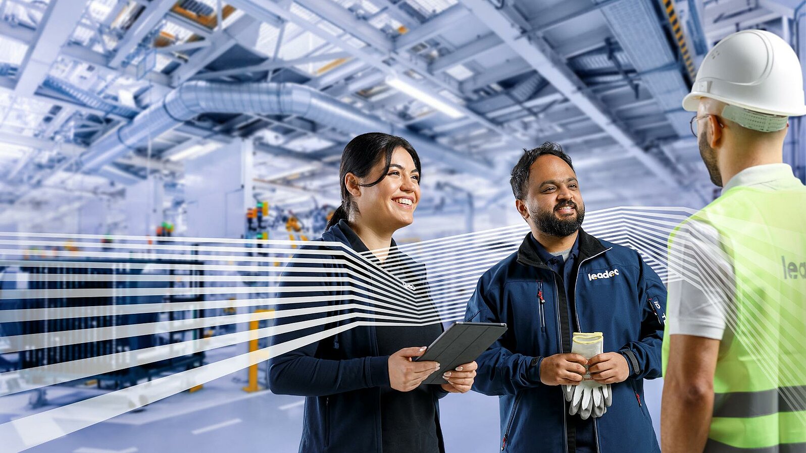 Three Leadec employees in workwear talking in front of a factory background.