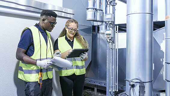 Two Leadec employees with check list and tablet at ventilation system on a factory roof.
